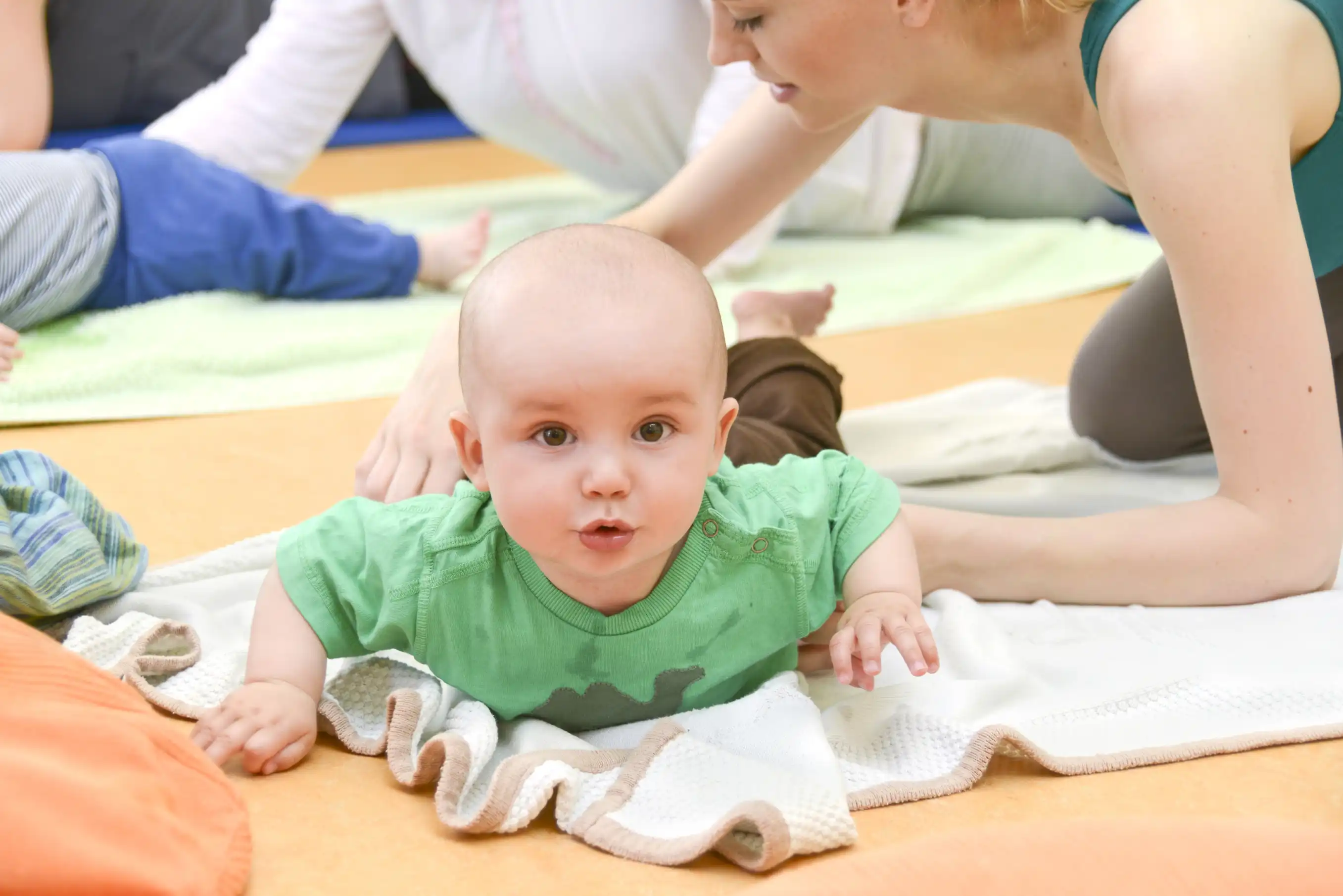 Baby lying on its stomach on top of a towel with its head up and the mother assisting it